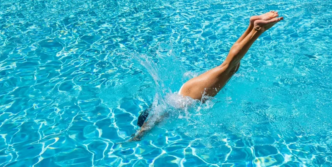 Eine Frau taucht kopfüber in einen klaren, blauen Pool ein, was an ein erfrischendes Sommerretreat erinnert.